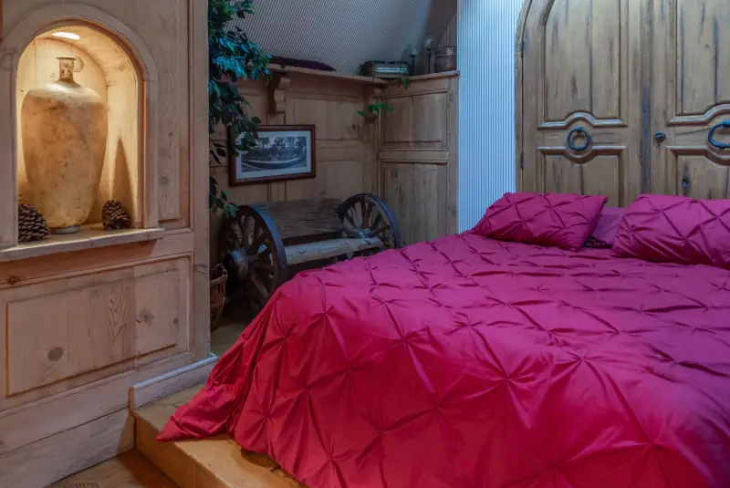 A bedroom with a deep red bedspread and an arched niche at The Enchanted Manor