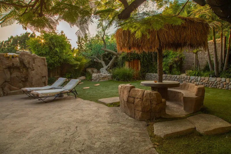 Sun loungers and a stone table under a palapa on the lawn at The Enchanted Manor