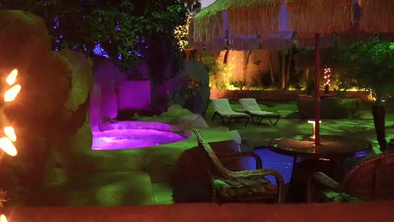 The raised Jacuzzi glowing violet under the palapas at The Enchanted Manor