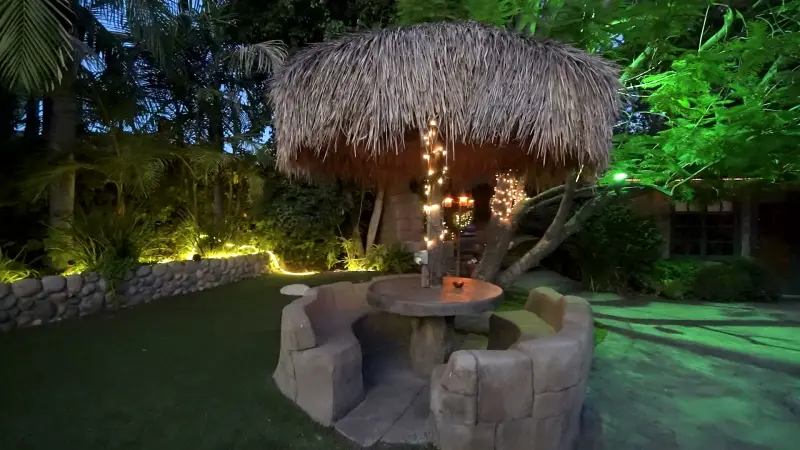 A thatched palapa strung with lights over a stone table at The Enchanted Manor