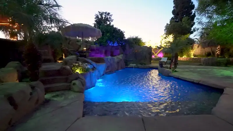 The pool lit blue beneath violet-lit rocks at The Enchanted Manor